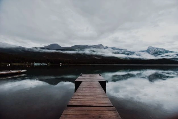 Boardwalk into a lake surrounded by cloudy mountains