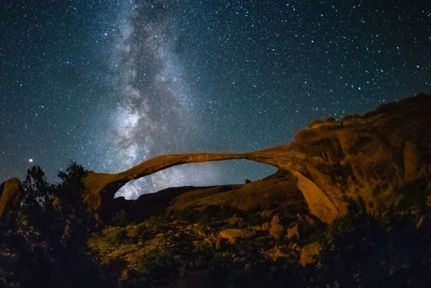 A night photo of stars and the milky way above a natural arch.